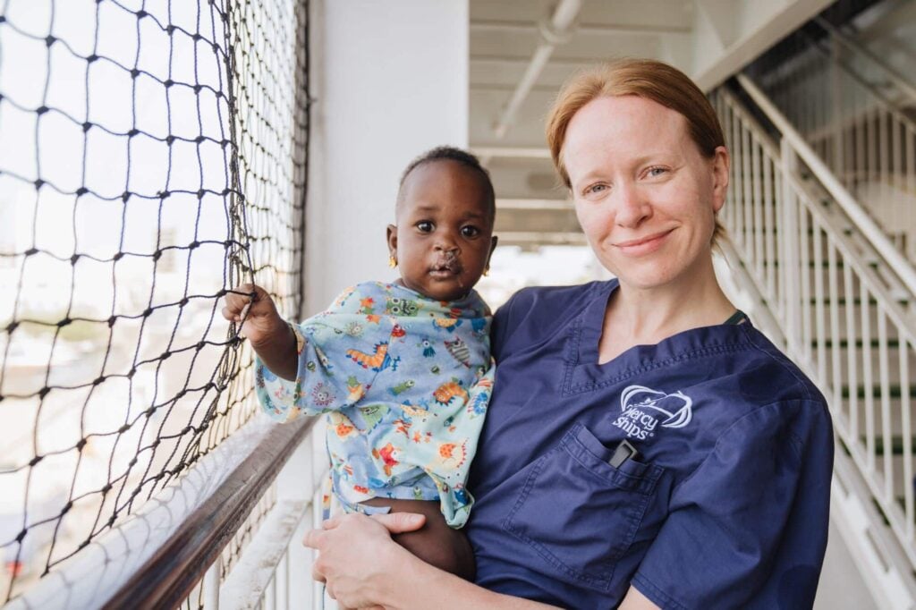 foto van een vrijwilliger van Mercy Ships met een kleine patiënt op haar arm