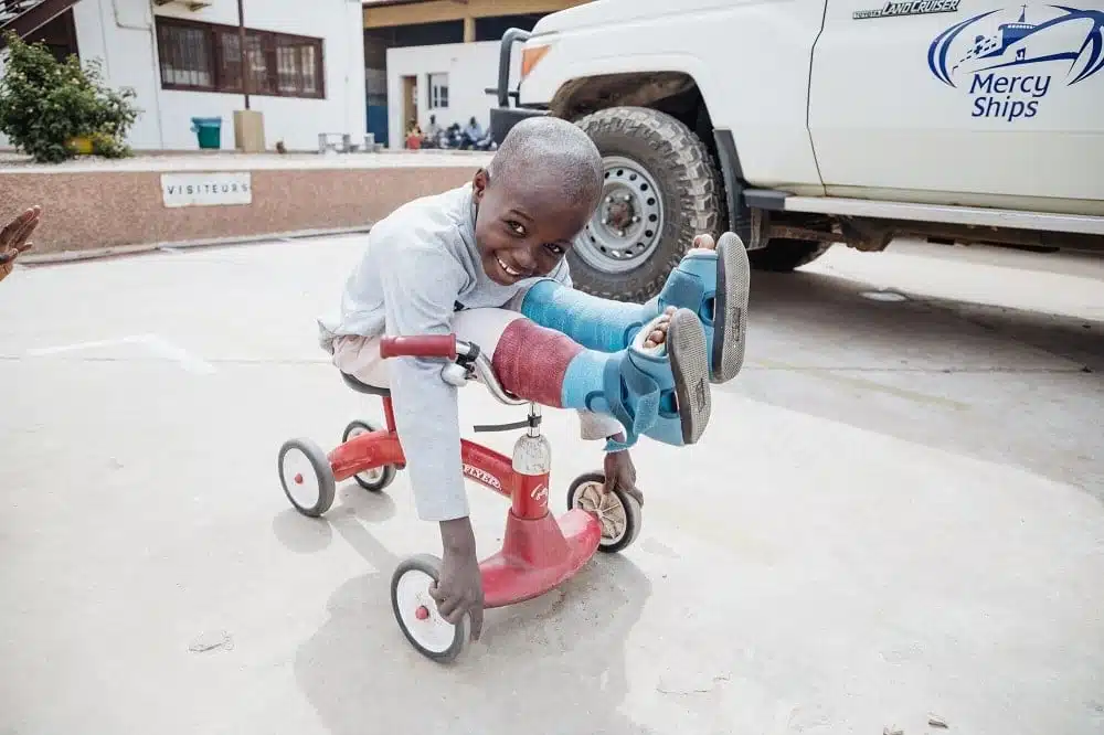 foto van een jongetje na een orthopedische operatie met twee benen in het gips op een fietsje