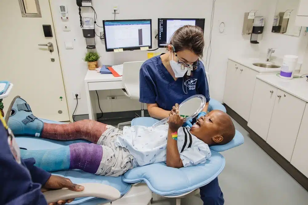Jongetje met zijn mond open op een tandartsstoel met een spiegel in de hand
